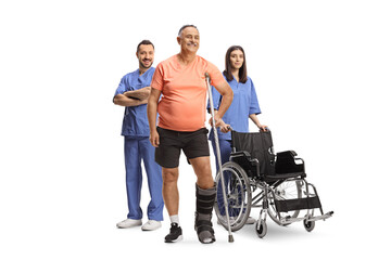Mature male patient with an orthopedic boot and crutch standing with health care workers