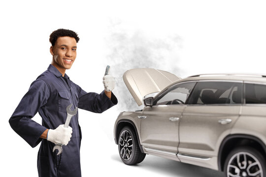 African American Car Mechanic Holding A Wrench And Gesturing Thumbs Up In Front Of A Broken Down SUV