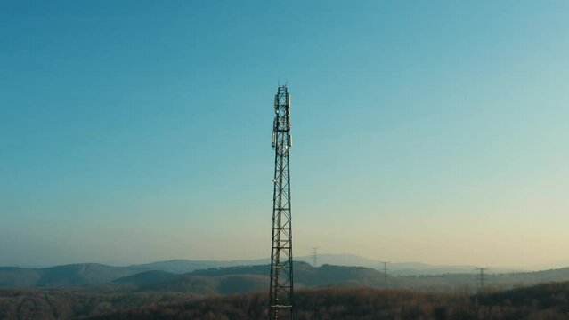 4K circling drone footage around telephone mast of cell tower. Aerial outlook of telecom antenna and cellular base station during golden hour stock video.	
