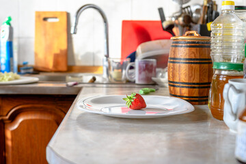 Fototapeta na wymiar Appetizing strawberries lie on a plate, on the kitchen table, against the background of the kitchen interior.
