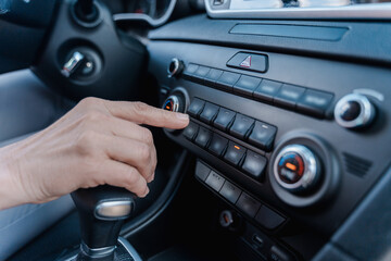 Close-up hand of a mature woman controlling air conditioner, touching the dashboard of a modern car