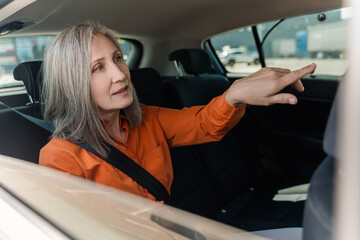 Caucasian mature adult woman 60s, sitting in back passenger seat of a taxi, talking to taxi driver
