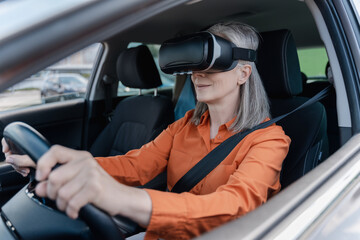 Confident portrait of a gray haired Caucasian senior woman 60 years old, wearing virtual reality glasses, holding hands on the steering wheel, driving a car with a fastened seat belt. Road insurance