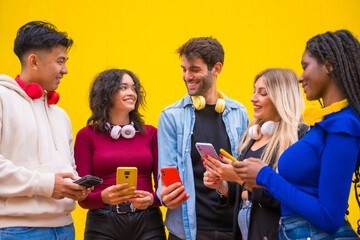 Obraz premium Low angle view of a group of smiling young multi ethnic teenage friends using cell phones on a yellow background. Technology addicted millennial community concept. Social Media communication
