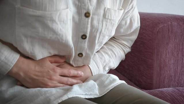 Female feel spasm stomach ache indoor. A view of female with spasms in her stomach suffer fro pain on the sofa.
