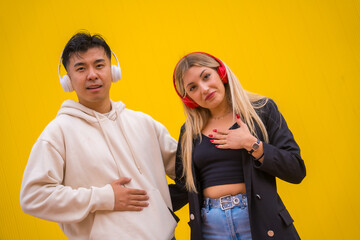 Portrait of multiethnic couple of Asian man and Caucasian woman on a yellow background, dancing bachata and salsa with headphones