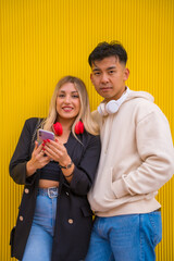 Portrait of multiethnic couple of Asian man and Caucasian woman on a yellow background, surfing the internet with the phone