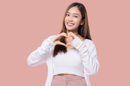 Beauty Asian woman making heart shape hand sign isolated on pink background.