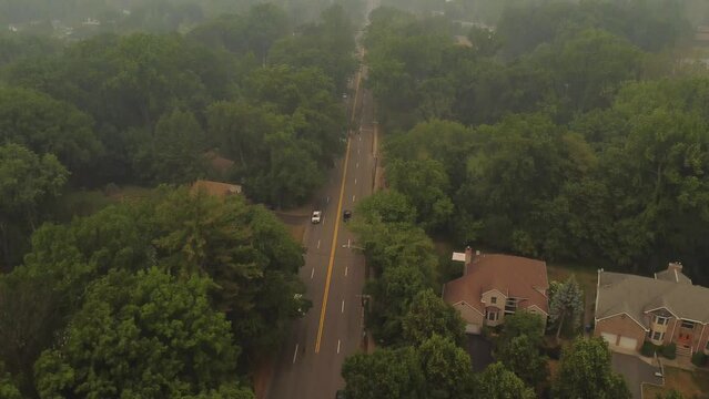 Aerial shot of cars driving on foggy suburban forest road