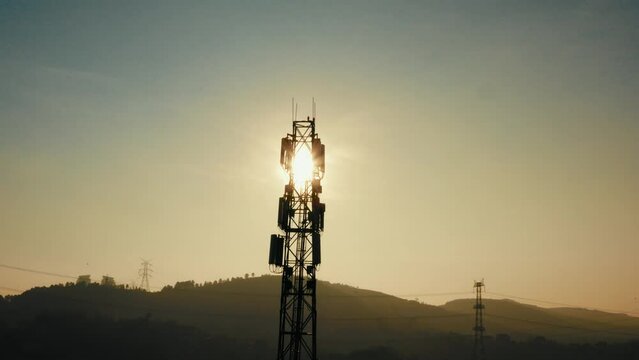 4K drone shot of cellular base station of cell tower. Aerial view of telecom antenna and telephone mast against sun with transmission towers in the background during golden hour stock video.
