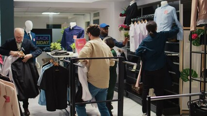 Black friday sales madness in clothing store, people emptying hangers and shelves to buy promotional items on discount. Crazy crowd of shoppers acting obsessed in shopping mall. Tripod shot.