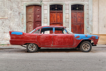 A side photo of American old car in Cuba in front of a facade with 3 doors 