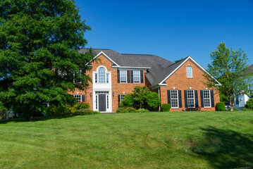 Large, beautiful, single-family brick country house. Large lawn and green trees.