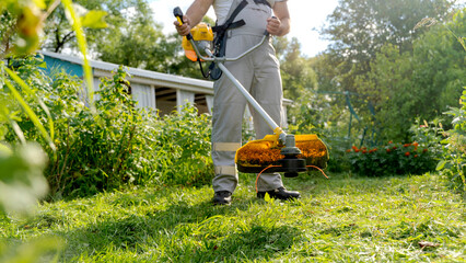 a man with a grass trimmer mows the lawn