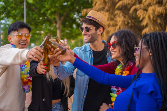 Group of multi ethnic friends at a party in a park having fun - Diverse young people toasting with glass bottles of beer at a summer party, youth concept