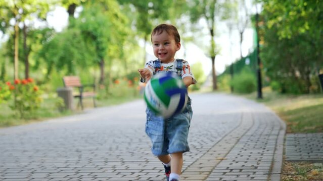 Smiling toddler boy throwing a ball happily. Adorable Caucasian child playing in the park in summer.