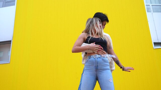 Multi-ethnic dance of an Asian and Caucasian couple dancing bachata on a yellow background