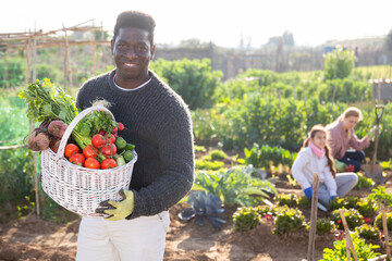 Portrait of a smiling African american man in a vegetable garden with a basket of crops in his hands