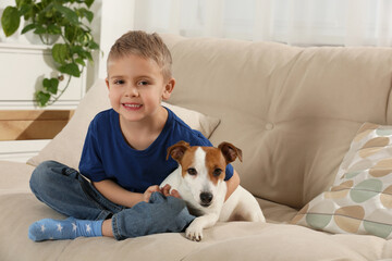 Little boy with his cute dog on sofa at home, space for text. Adorable pet