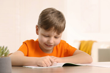 Naklejka premium Little boy erasing mistake in his notebook at wooden desk indoors