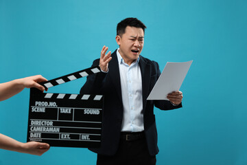Emotional asian actor with script performing while second assistant camera holding clapperboard on...