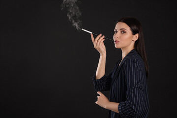 Obraz premium Woman using long cigarette holder for smoking on black background, space for text
