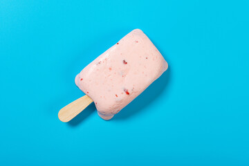 top view fresh strawberry flavor popsicle starts melting on a blue background