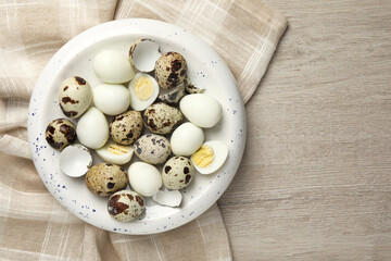 Unpeeled and peeled hard boiled quail eggs in bowl on white wooden table, top view. Space for text