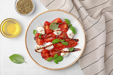 Tasty salad Caprese with mozarella balls, tomatoes, basil and other ingredients on white tiled...