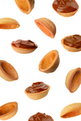 Many empty and filled with caramelized condensed milk nut shell shaped cookie parts falling on white background