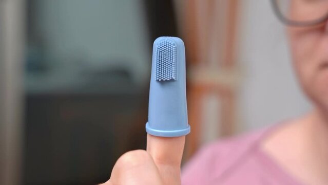 Children tooth silicone, rubber brush on the finger for massaging the gums of babies. Close-up mother holds a brush for newborns twists, examines. Modern child care products, hygiene