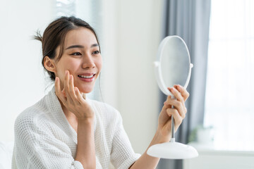 Asian beautiful woman looking at the mirror after apply lotion on face.