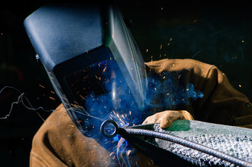 A man in a welding helmet welds a piece of metal and concrete sculpture