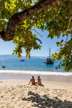 casal sentado sobre a arreia da praia aproveitando a tarde ensolarada na linda praia de Paraty. Casal em Lua de Mel. 