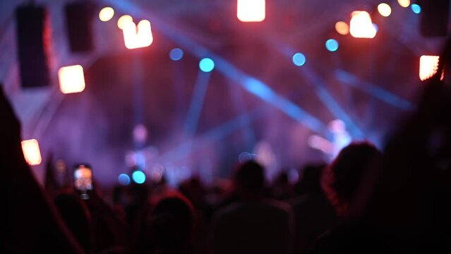 Blurred silhouettes of people raise hands in front of colorful lights in concert