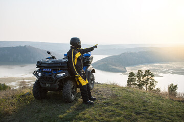Man is watching the sunset from the mountain standing near ATV. Offroad travel adventure trip expedition.