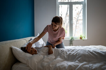 Childrens health. Worried European woman mother checking temperature of sick daughter lying in bed with fever, caring mom parent taking care of child with cold at home