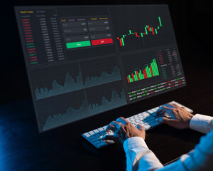 Caucasian man sits in the dark in front of a virtual screen. Stock exchange charts. Close-up of male hands on the keyboard.