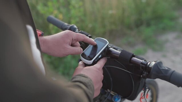 Cyclist use bicycle computer on handlebars of mountain bike in nature. Traveler on cycle looks at map, builds route using GPS on bicycle navigator. Activity tracker and offline maps for bike rides.