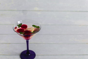 summer cocktail with lemon, mint and red ice cubes in a transparent martini glass on a light background