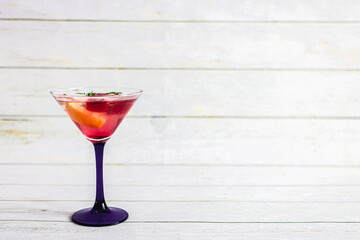 summer cocktail with lemon, mint and red ice cubes in a transparent martini glass on a light background