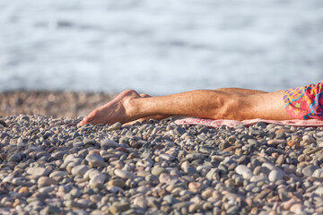 men's legs lying on a towel on a pebble beach against the background of the sea