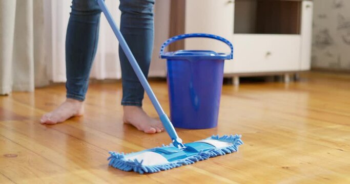 Woman in casual clothes washing a wooden floor with a damp microfiber mop