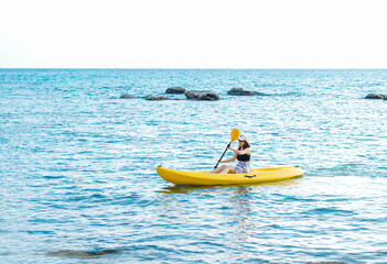 Fototapeta na wymiar Happy Asian woman in black tank top and cap kayaking on yellow kayak boat with using paddle on the sea. Happy female having fun activity on seascape view background, Holiday trip vacation.