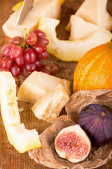 Cheese plate served with grapes, melon, figs, crackers, honey, nuts and white wine on a wooden table