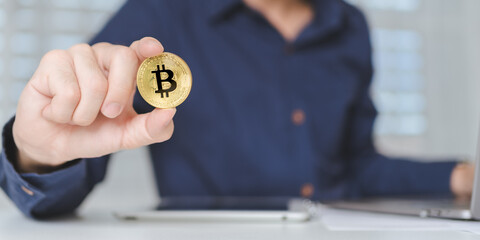 Bitcoin Cryptocurrency investment concept. Trader or investor hand holds Bitcoin Cryptocurrency gold coins. Businessman shows Bitcoin Cryptocurrency on hands while using laptop for trading. Banner. - 613036919