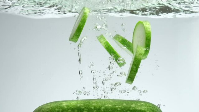 A green Winter melon (Benincasa hispida) with several winter melon slices falling into transparent water. Slow motion shot of fresh vegetables