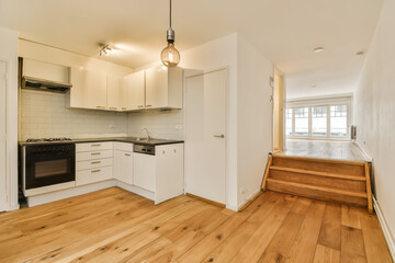 an empty kitchen with wood flooring and white cupboards on either side of the door to the living room