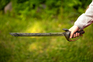 The child's hand holds a pirate saber.Summer games for children in the fresh air.Saber fighting.A...