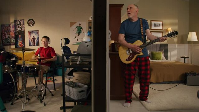 Young boy practices musician skills uses drum kit. Elderly man sings and plays on electric guitar with neighbour. Thin walls and low level of sound insulation. Neighbors play music together. Zoom out.